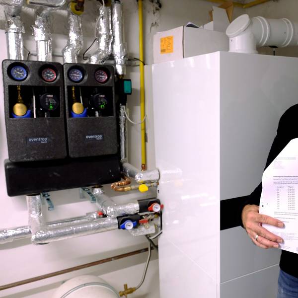 Andreas Kläser steht an seiner Heizungsanlage. In der Hand hält er Rechnungen des Energieversorgers e-regio.