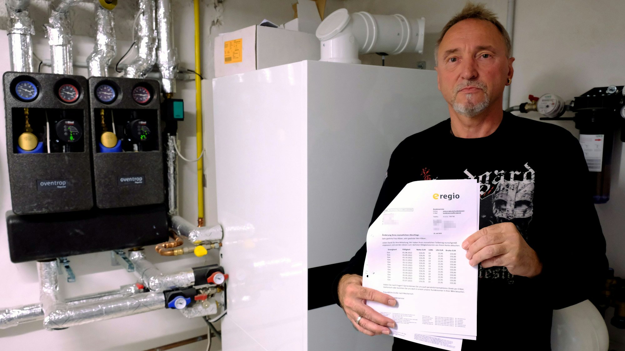 Andreas Kläser steht an seiner Heizungsanlage. In der Hand hält er Rechnungen des Energieversorgers e-regio.