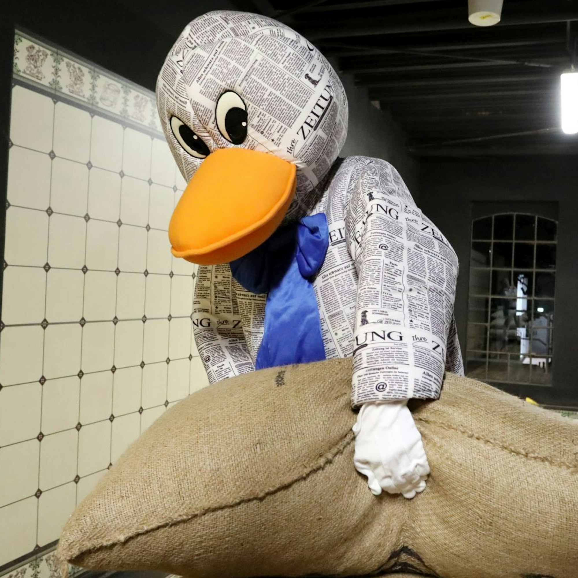 Die Zeitungsente Paula Print versucht, einen großen Jutesack hochzuheben, in dem Kakaobohnen sind.