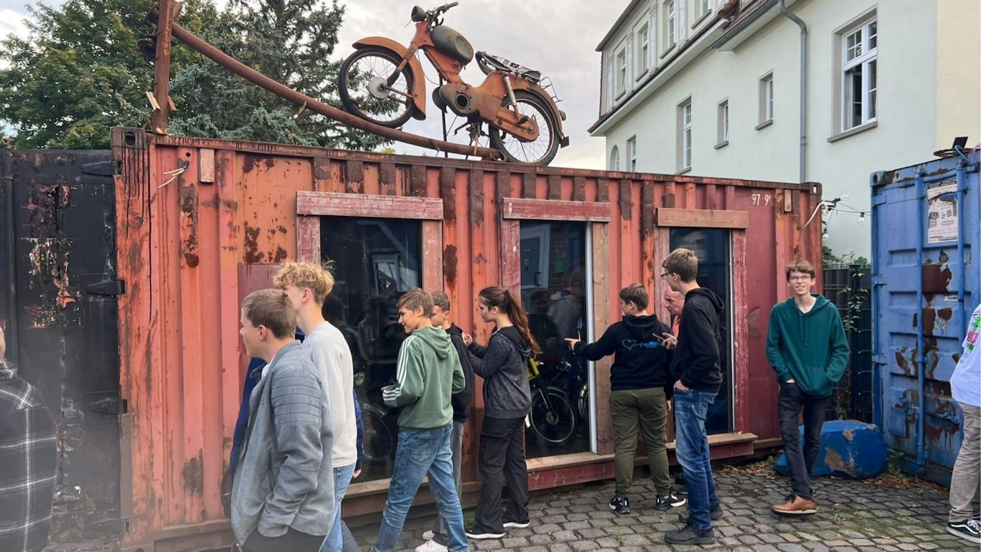 Die Jugendlichen der Realschule Bad Münstereifel besuchen das Mofa-Museum in Brühl. Sie stehen vor einem rostigen Container und schauen durch Scheiben hinein.