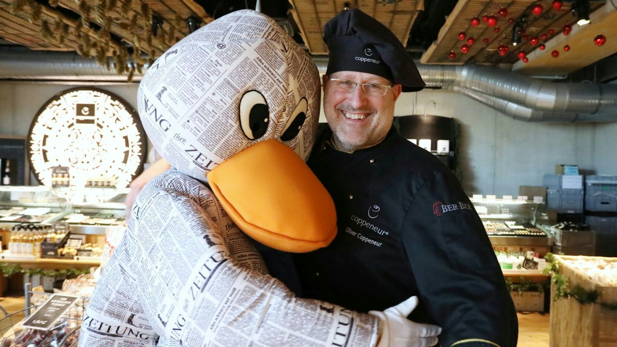 Das Zeitungsmaskottchen Paula Print umarmt den lachenden Chocolatier Oliver Coppeneur.