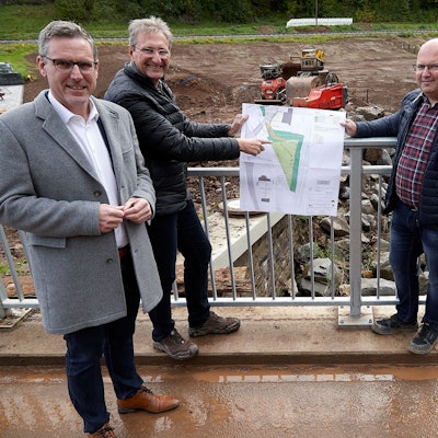 Mit einem Plan zeigen die drei auf einer Brücke, welche Maßnahmen getroffen werden.