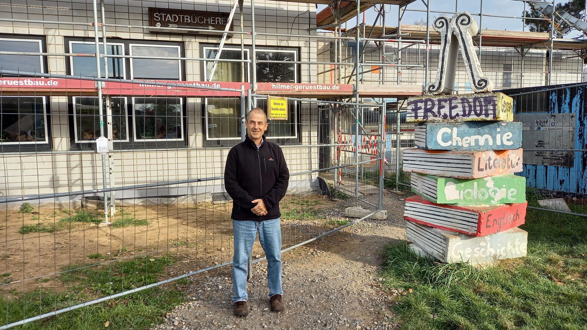Ein Mann steht vor einem eingerüsteten Gebäude.