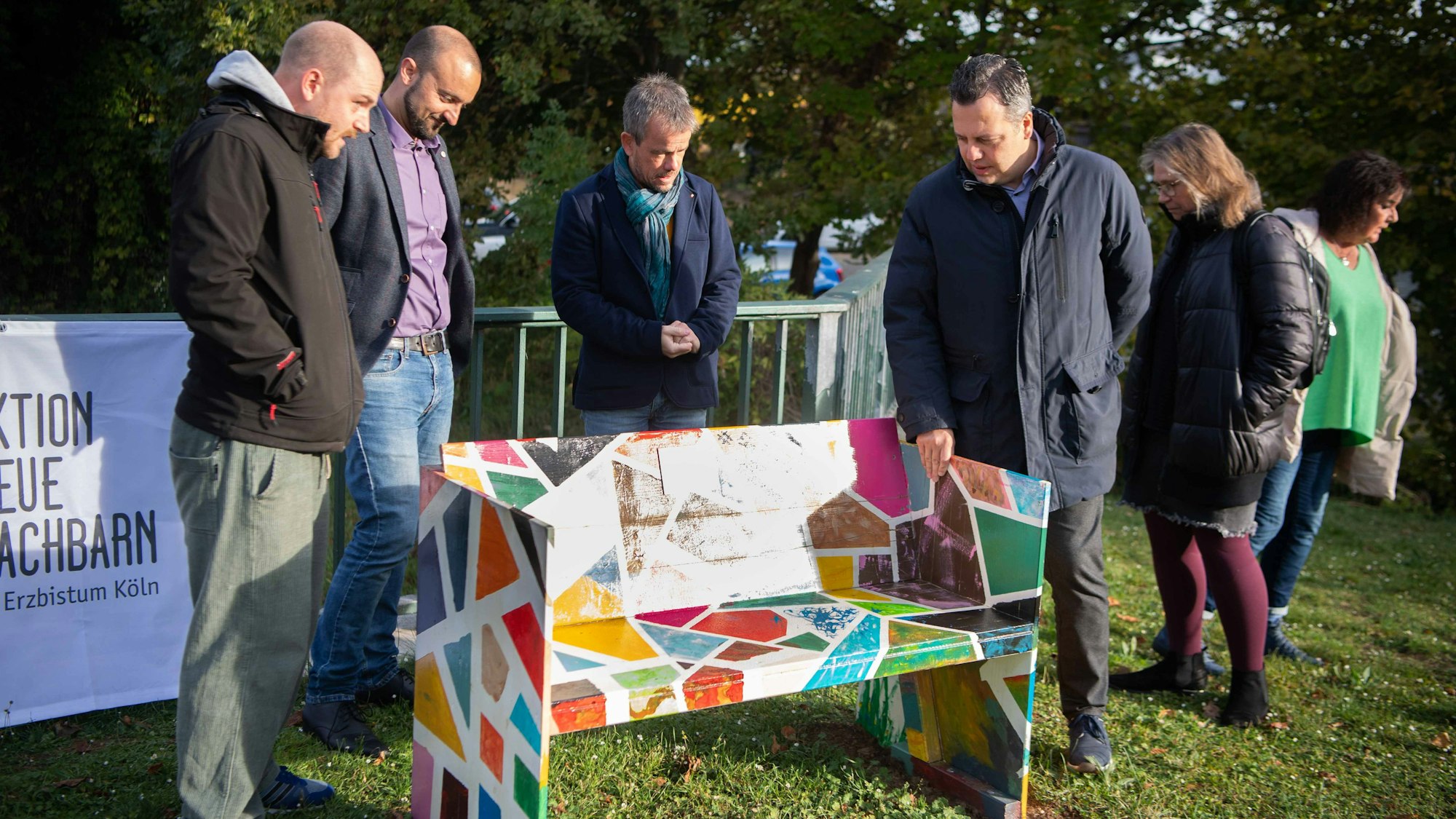 Das Bild zeigt Mitarbeiter der Caritas Euskirchen und Bürgermeister Sacha Reichelt, wie sie sich die renovierte Bank begutachten.