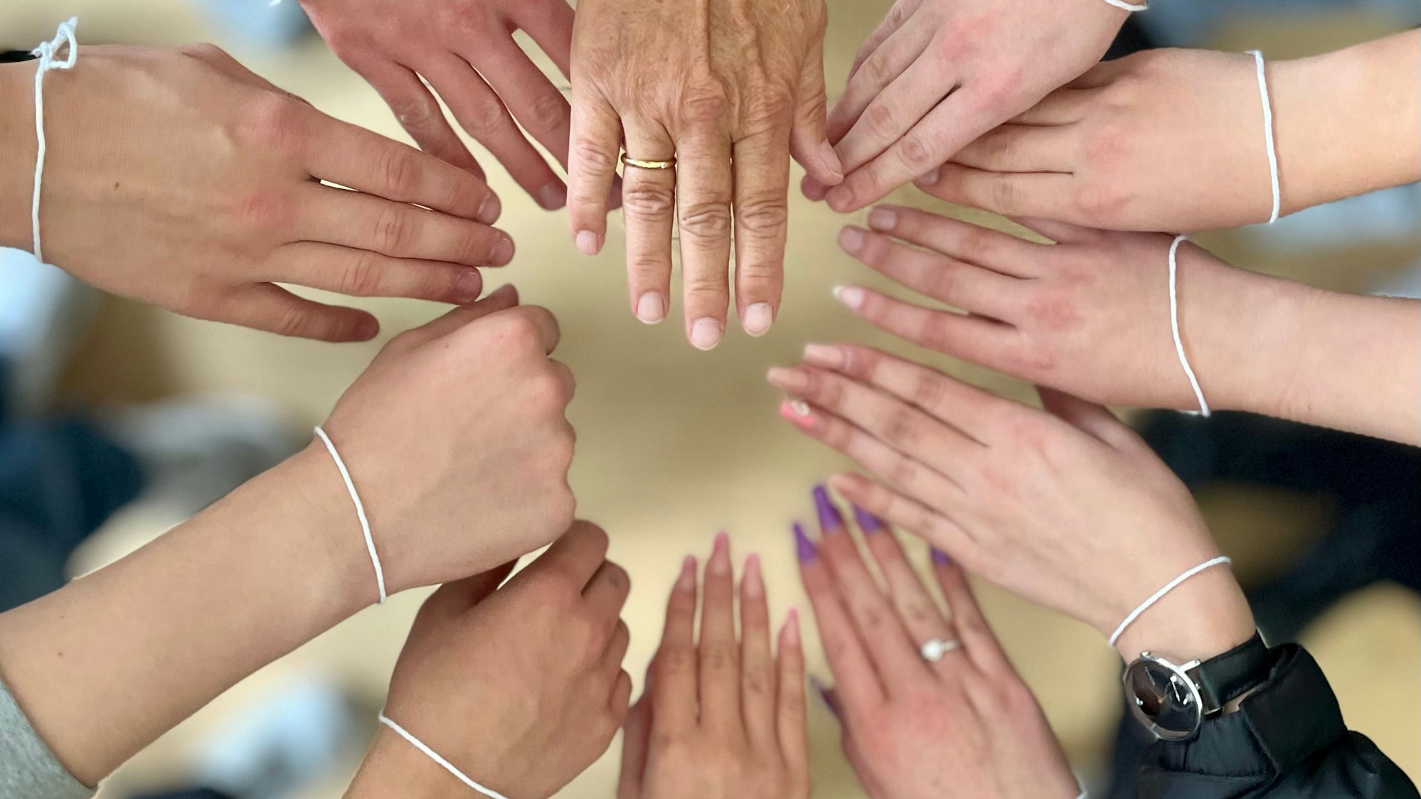 Viele Hände mit weißen Bändchen am Gelenk werden zusammengehalten.