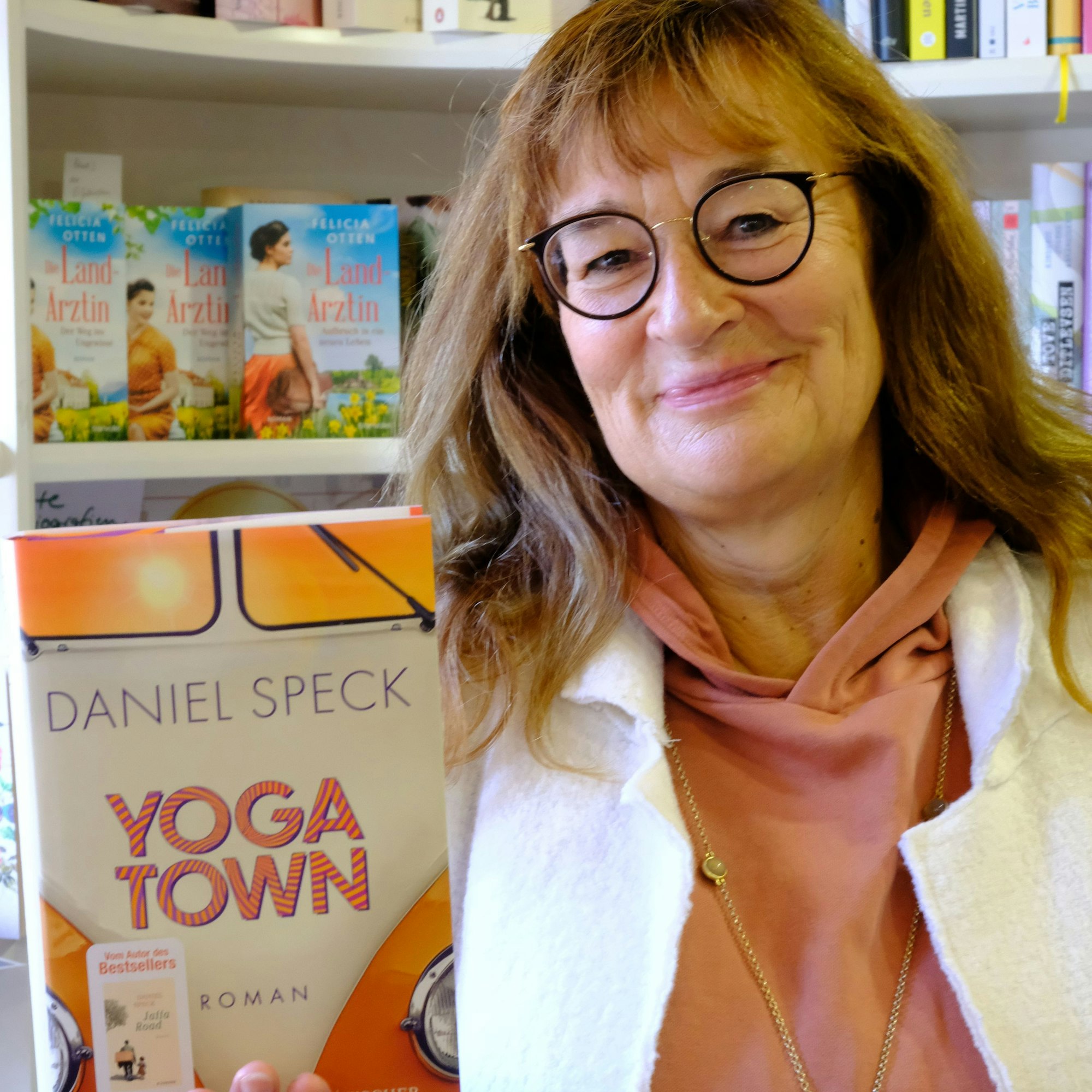 Renate Elsen steht mit einem Buch vor einem Regal.