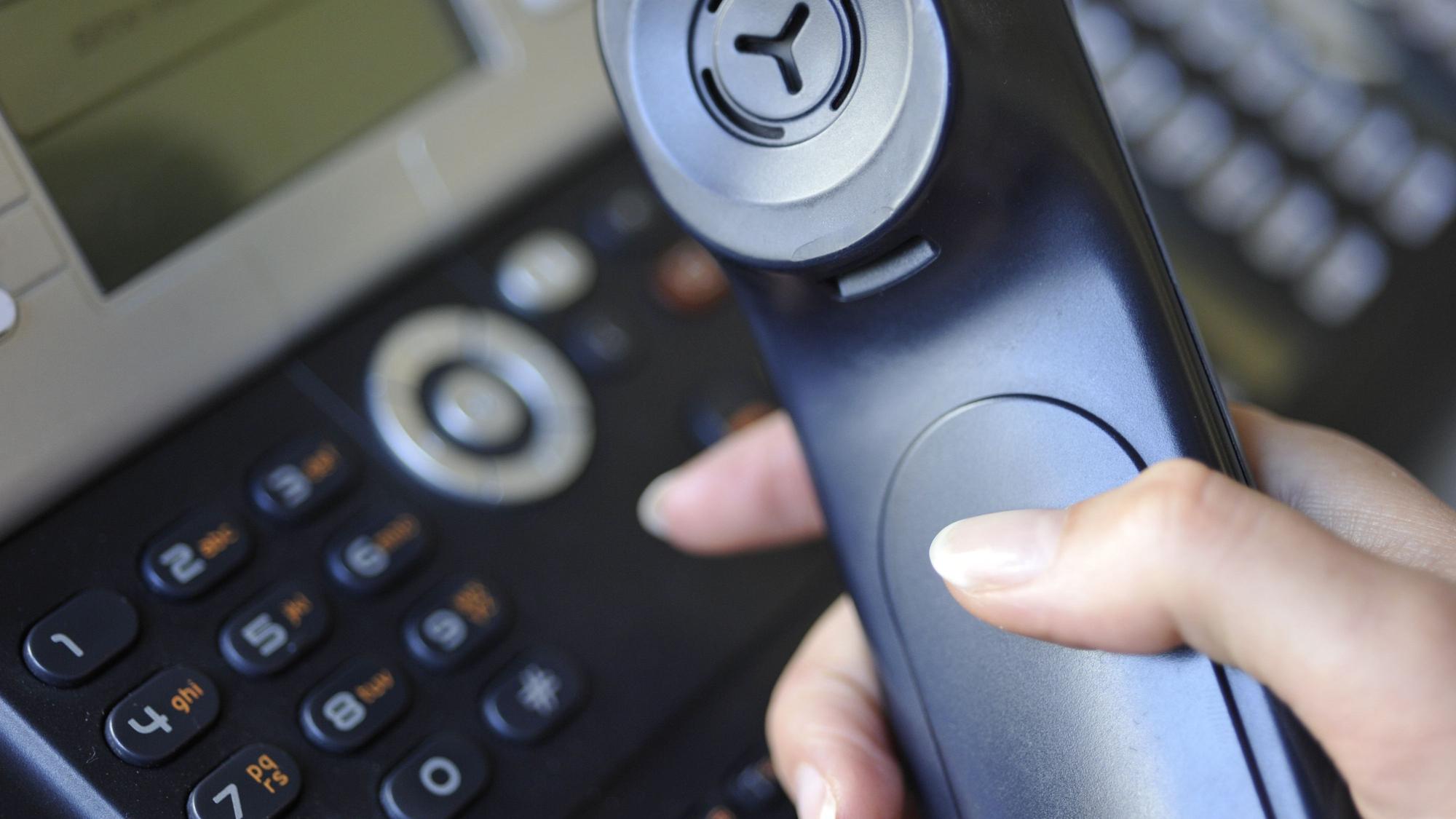 Eine Frauenhand hält einen Telefonhörer und wählt eine Nummer.