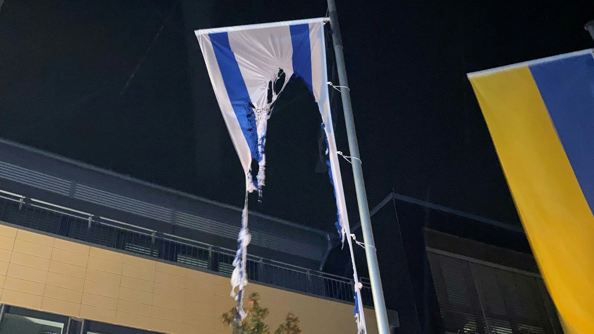 Die Reste einer israelischen Flagge, die an einem Fahnenmast vor dem Rathaus in Mechernich hängt, ist zu großen Teilen verbrannt. Daneben ist eine ukrainische Fahne zu sehen.