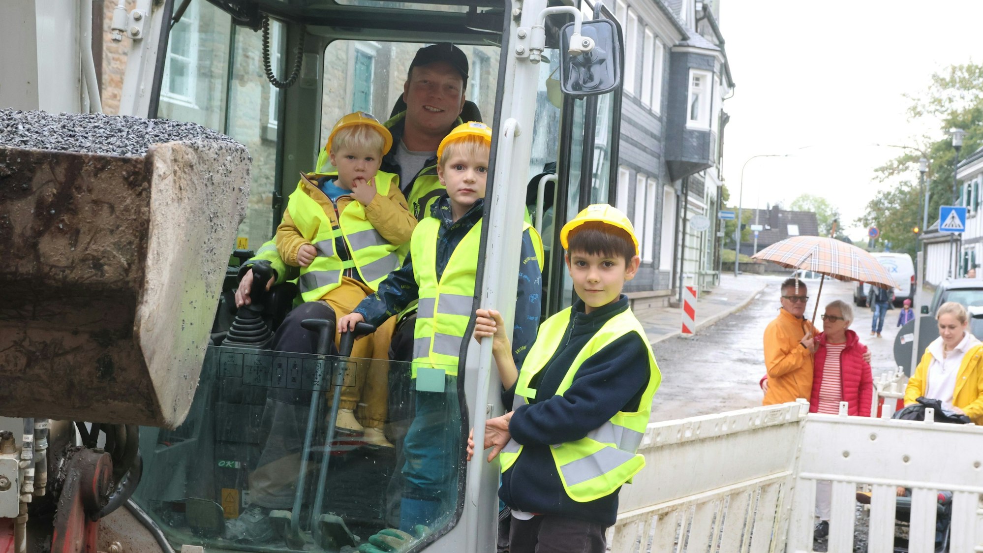 Drei Jungs sitzen mit einem Baggerfahrer auf einem Bagger.