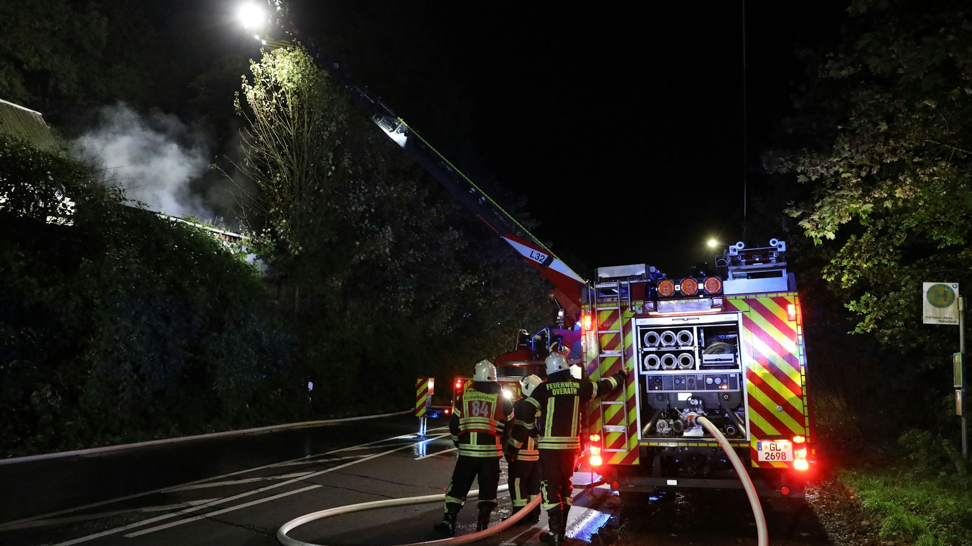 Ein Feuerwehrfahrzeug steht auf einer Straße. Von dieser wird mit einer Drehleiter das Feuer in einem nahen Gebäude gelöscht.