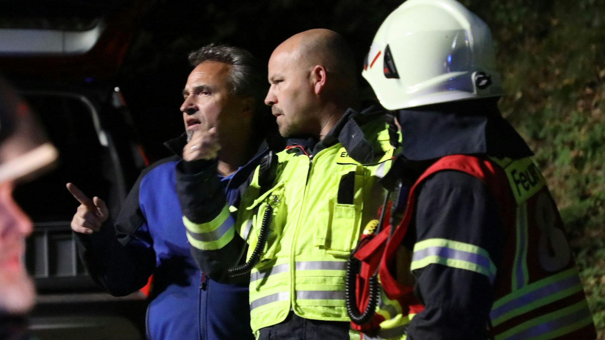 Drei Einsatzkräfte von Feuerwehr und Energieversorger stehen im Scheinwerferlicht und sprechen miteinander.