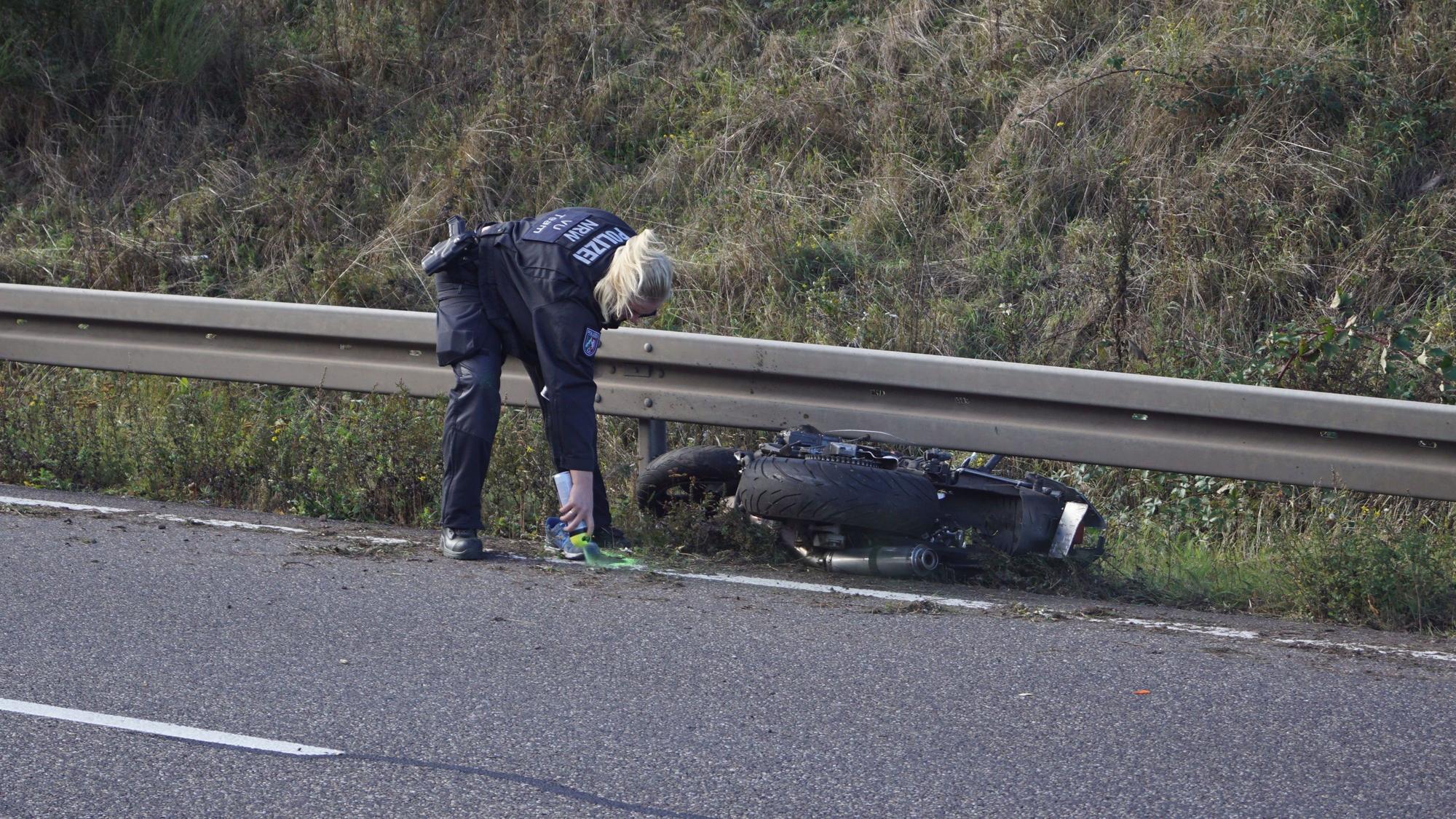 Eine Polizistin markiert nach einem Unfall mit Sprühfarbe eine Stelle auf der B266 bei Mechernich-Firmenich. Ein Motorrad liegt unter einer Leitplanke.
