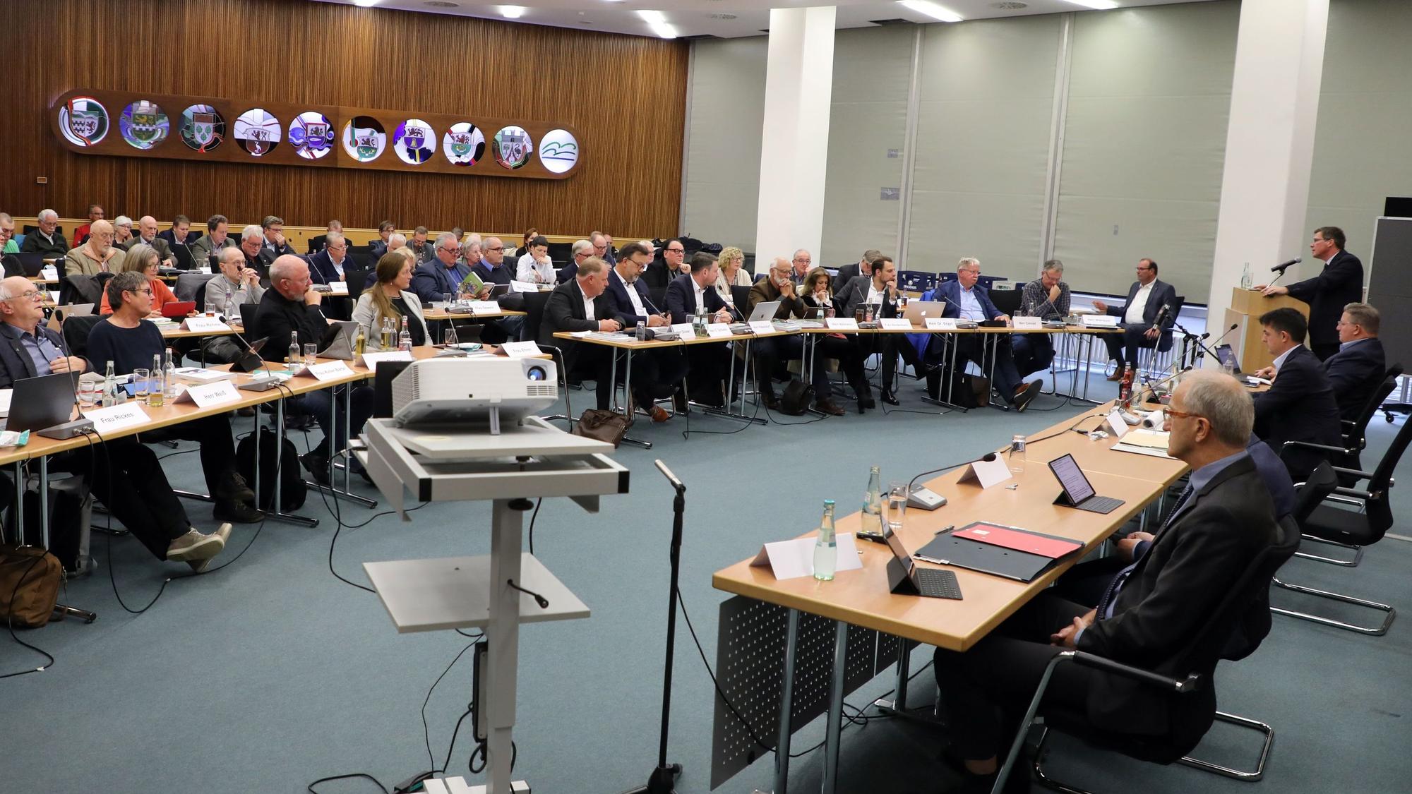 Im großen Sitzungssaal des Kreishauses Amt Rübezahlwald sitzen die Kreistagsmitglieder und die Verwaltung an Tischen.
