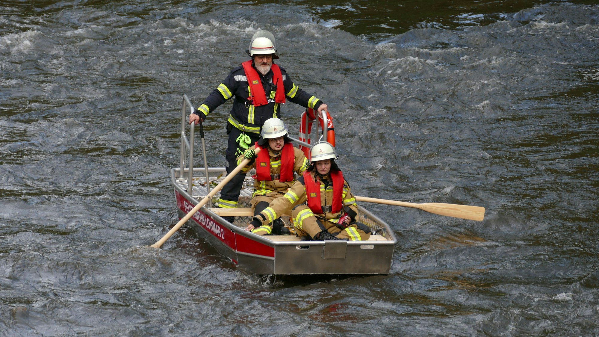 Drei Feuerwehrhelfer in einem Ruderboot.