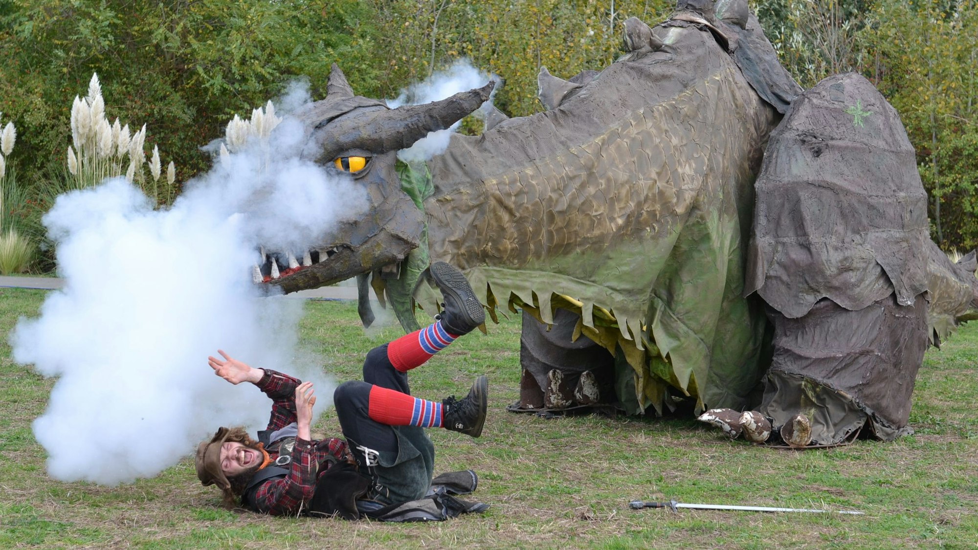 Der Darsteller von Räuberhauptmann Ronny liegt auf dem Boden vor der Figur eines Drachen, der Rauch ausstößt.