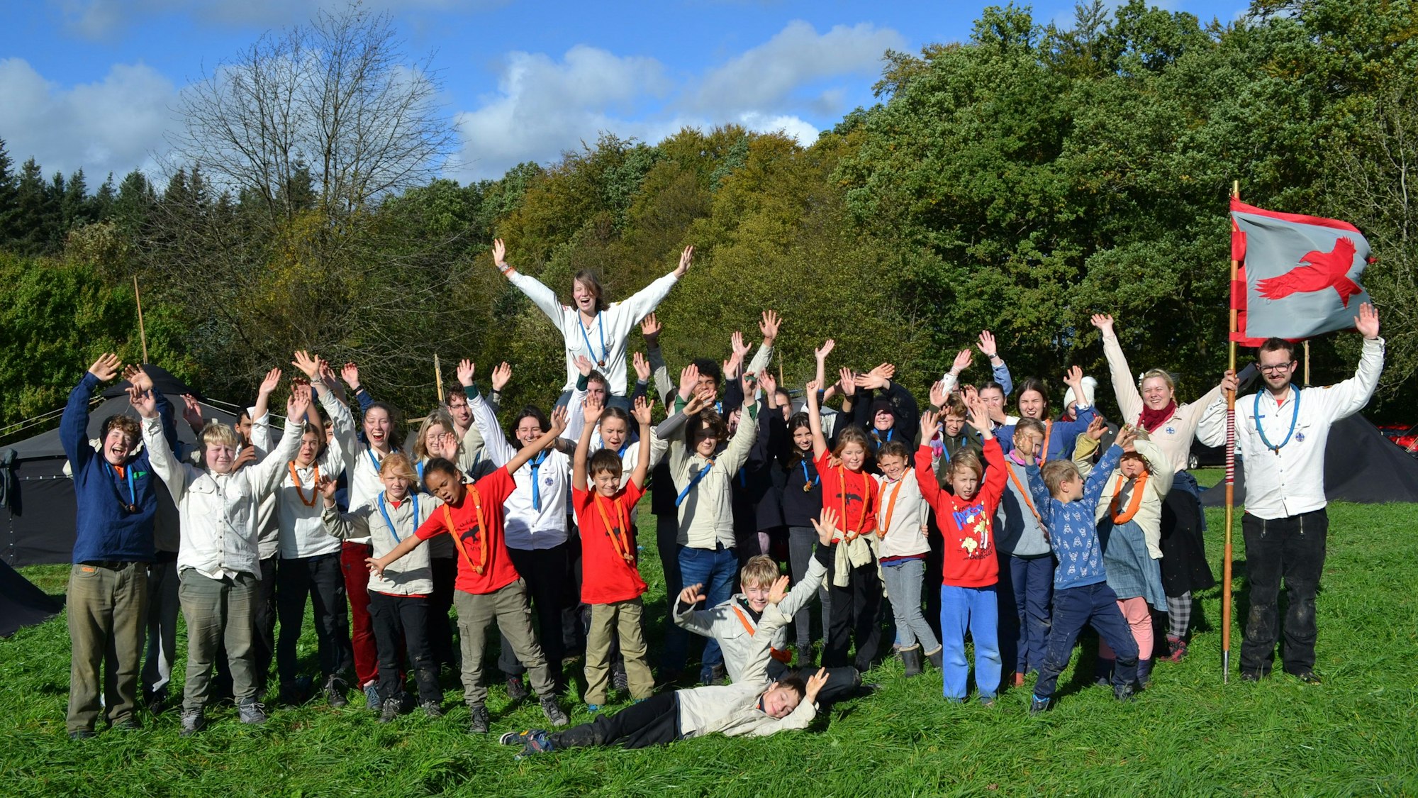 Kinder und Jugendliche, teilweise in Pfadfinderkluft, auf einer Wiese; im Hintergrund Herbstwald
