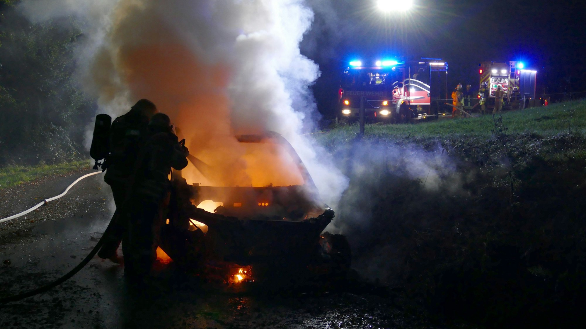 Rauchende Trümmer auf einer grünen Wiese. Im Hintergrund Feuerwehrfahrzeuge mit Blaulicht.