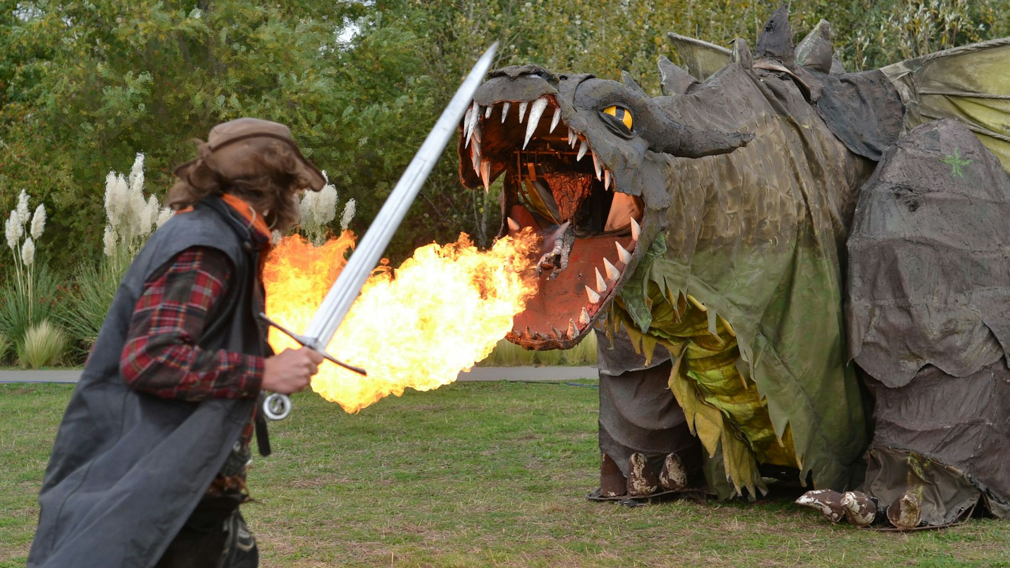 Ein Schwertkämpfer nähert sich der Figur eines feuerspeienden Drachen.