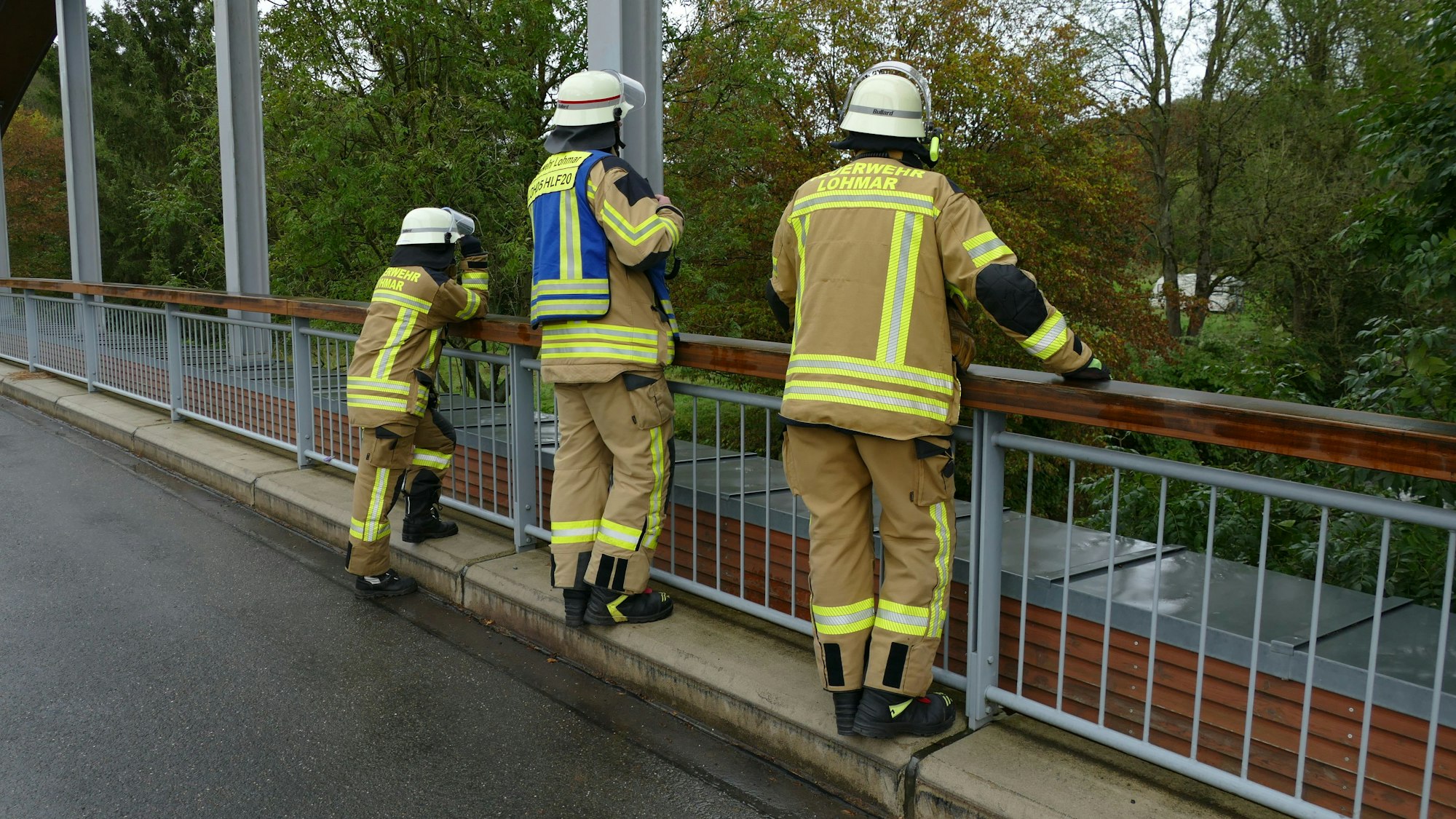 Drei Feuerwehrleute auf einer Brücke schauen ins Wasser.