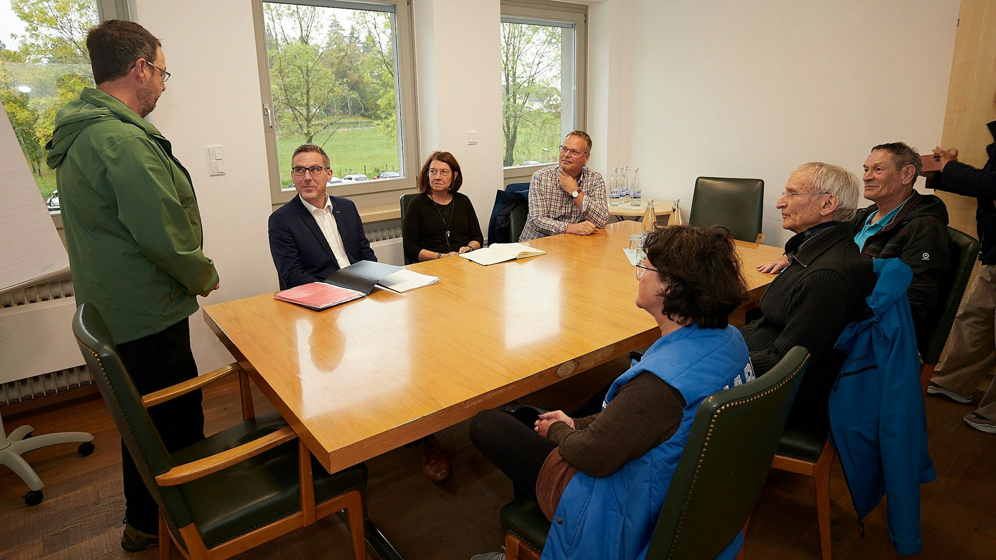 Vier Männer und zwei Frauen sitzen an einem Tisch im Zingsheimer Rathaus. Dr. Stefan Klose steht, er schaut den neben ihm sitzenden Bürgermeister Norbert Crump an.