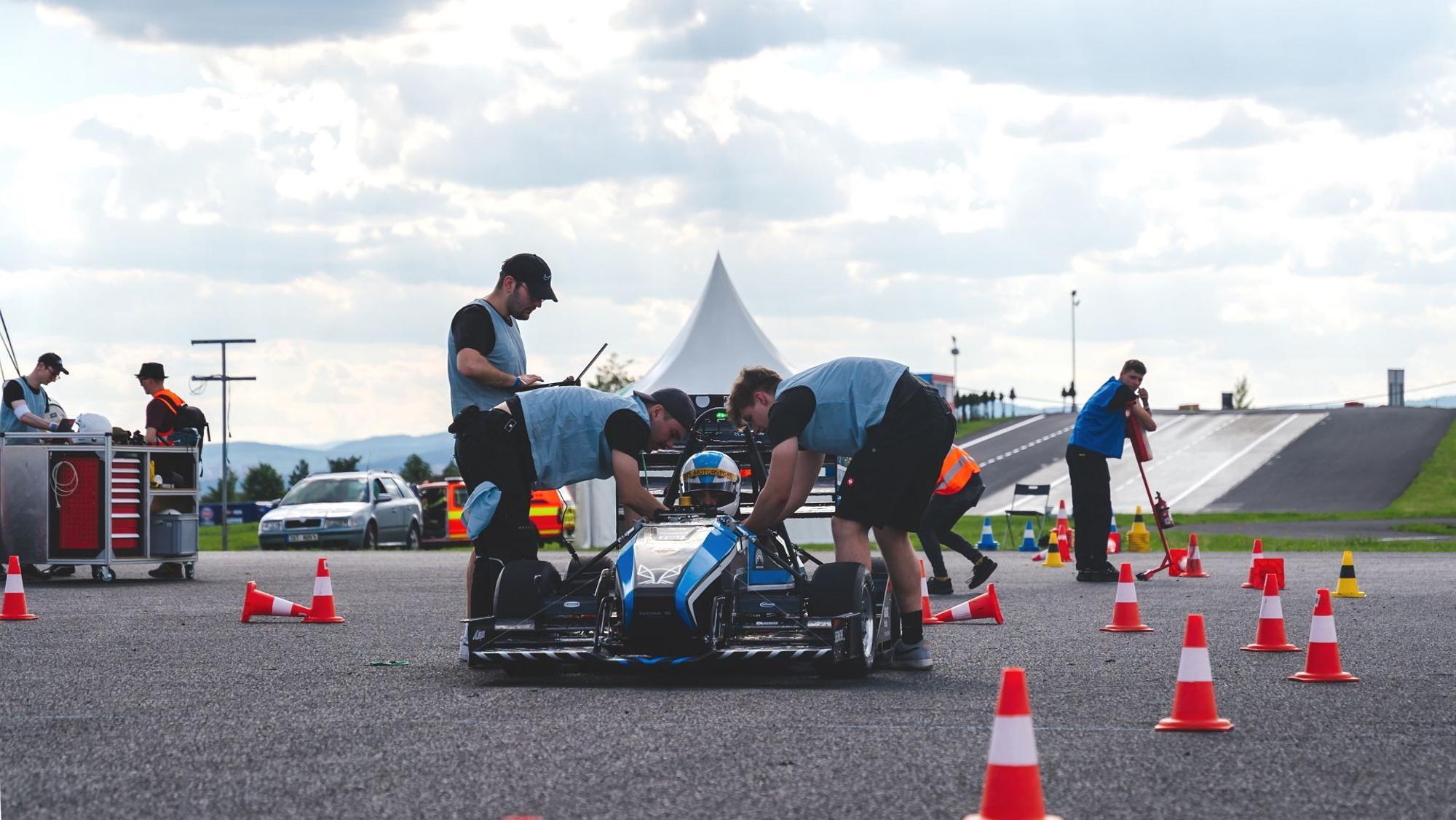 Mechaniker des Rennteams aus Sankt Augustin kümmern sich um das blaue Fahrzeug.