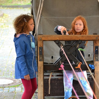 Zwei Mädchen stehen auf dem Handwerkermarkt in Kommern am Stand des Seilers und probieren die alten Geräte aus.