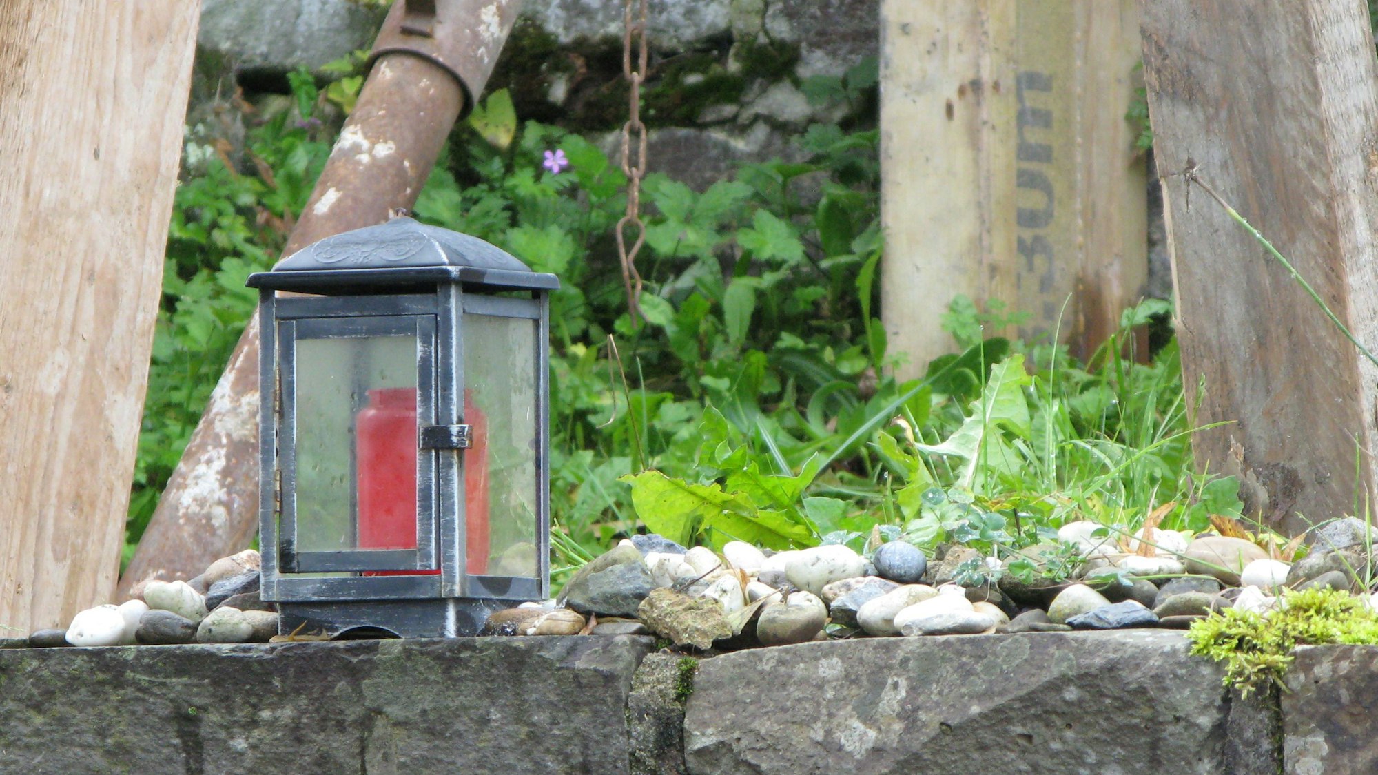 Auf der Krone einer Bruchsteinmauer der Synagoge stehen eine Laterne mit roter Grabkerzen, daneben befinden sich abgelegte Kieselsteine.