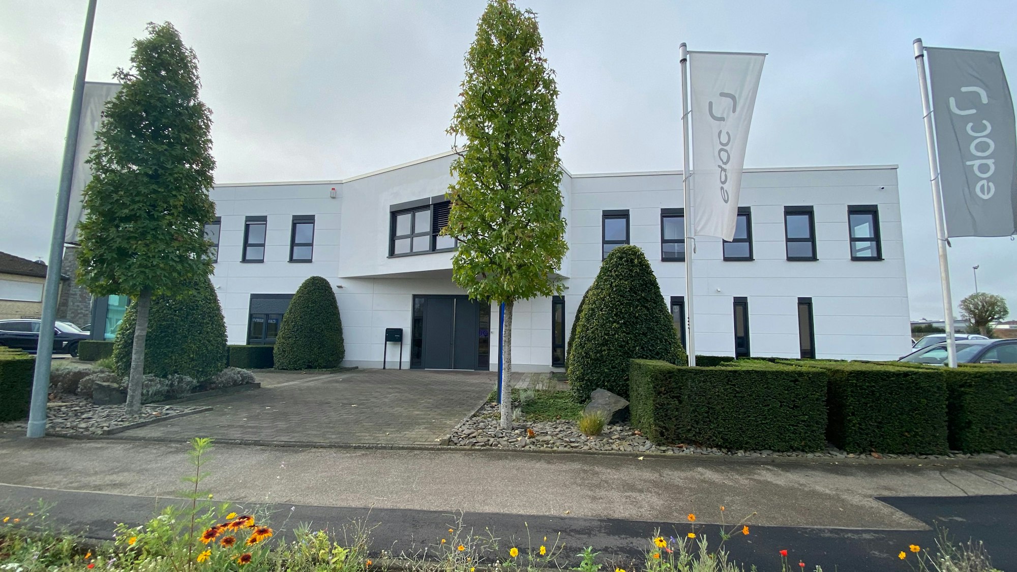 Der weiße Gebäudekomplex, in dem aktuell die Firma edoc ansässig ist, befindet sich an der Metternichstraße 4 in Weilerswist. Fahnen tragen den Schriftzug der Firma.