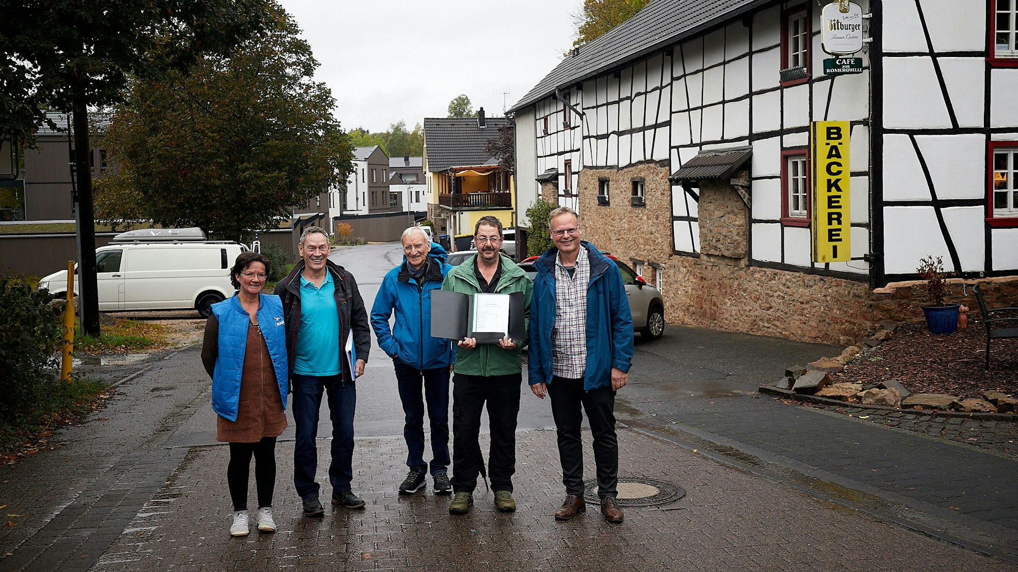 Vier Männer und eine Frau stehen auf einer Straße in Nettersheim an einem Fachwerkhaus. Ein Mann hält eine Mappe mit einer Unterschriftensammlung in der Hand.