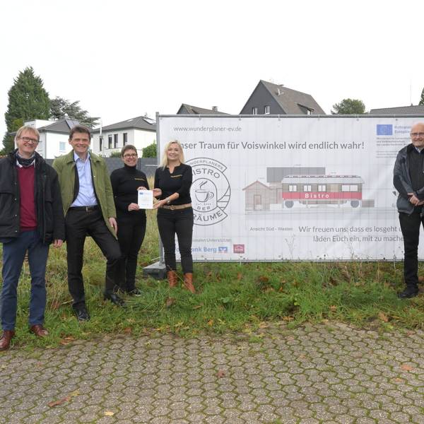 Menschen vor einem Plakat, das einen Zirkuswagen zeigt, der zu einem Café umgebaut werden soll.