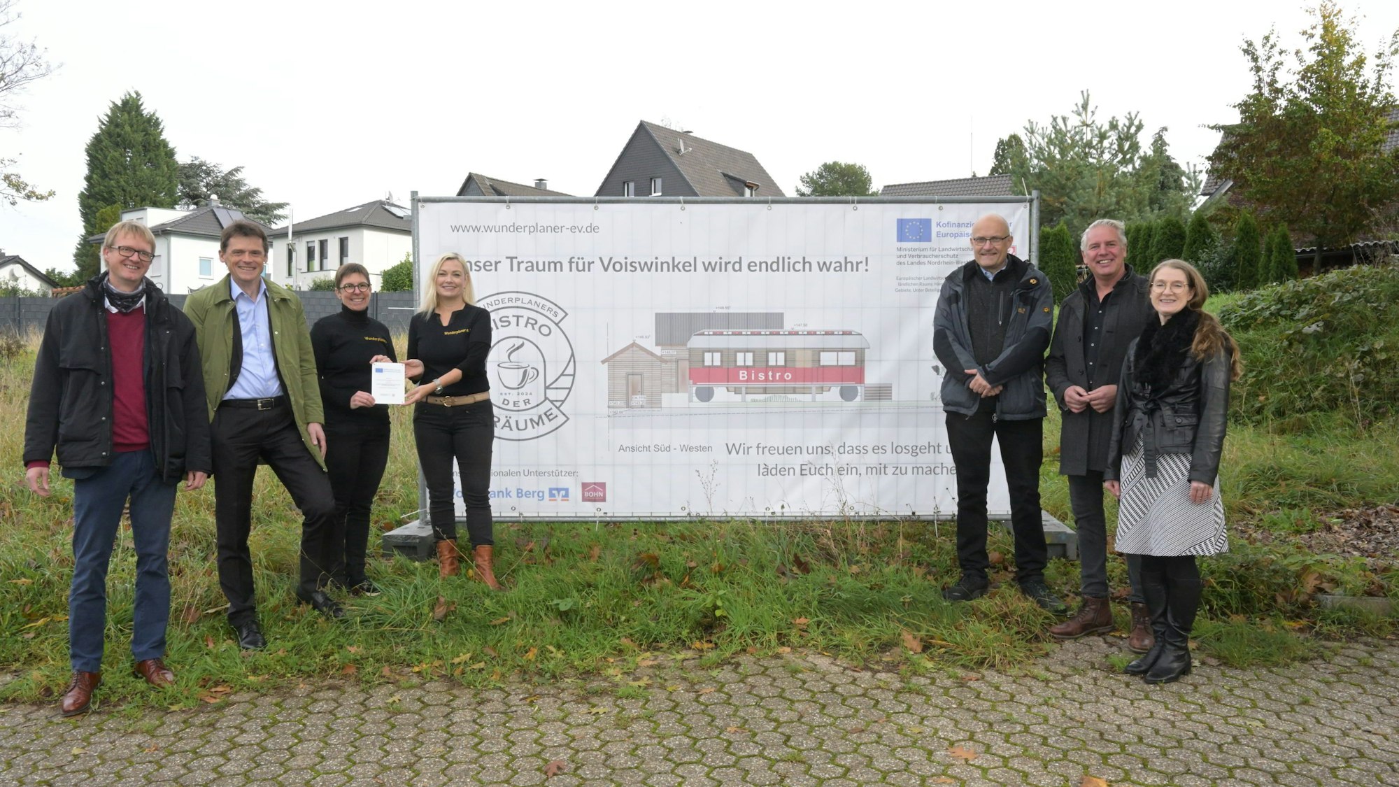 Menschen vor einem Plakat, das einen Zirkuswagen zeigt, der zu einem Café umgebaut werden soll.