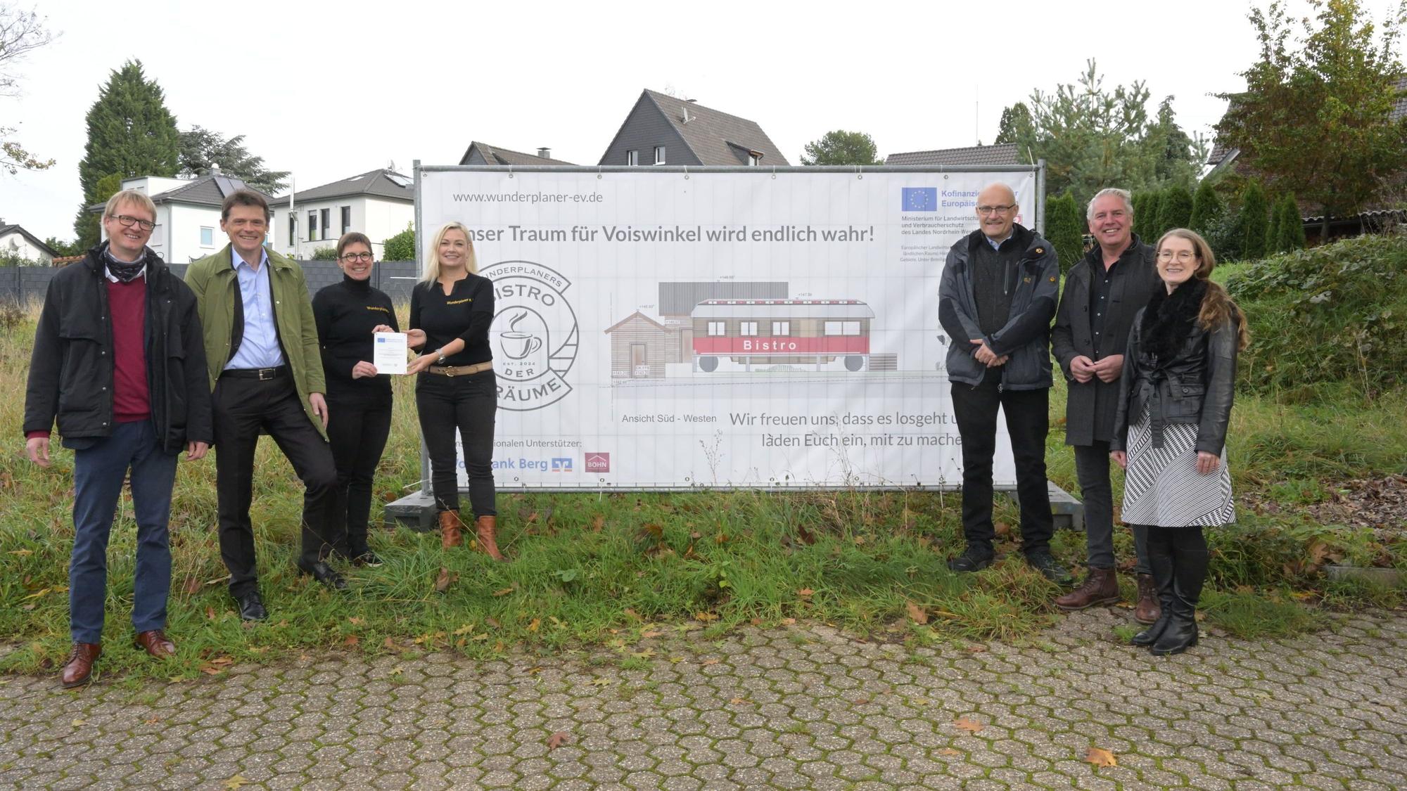 Sieben Männer und Frauen stehen vor einem Wiesengrundstück. Davor ein Plakat mit der Aufschrift: "Unser Traum für Voiswinkel wird endlich wahr!"