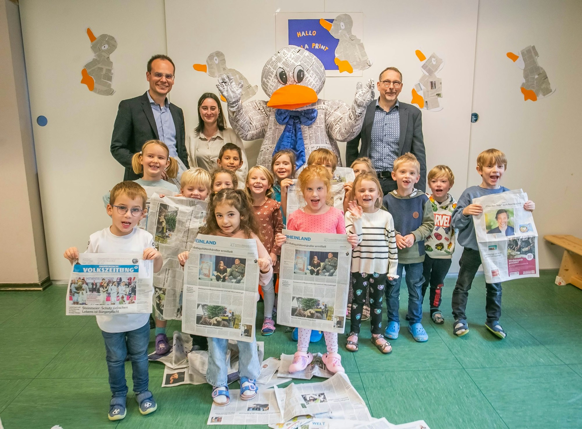 Kinder der Vorschulgruppe stehen mit Zeitungsausgaben und Erwachsenen mit dem Maskottchen Paula Print zusammen.