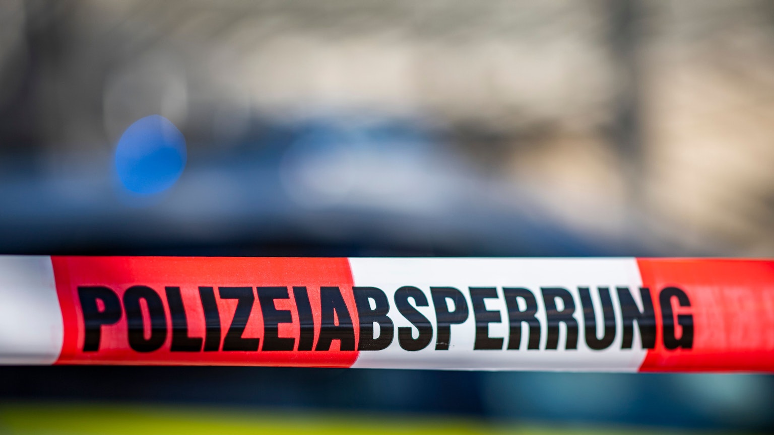 Ein Absperrband mit der Aufschrift „Polizeiabsperrung“ ist vor einem Polizeiwagen aufgespannt.