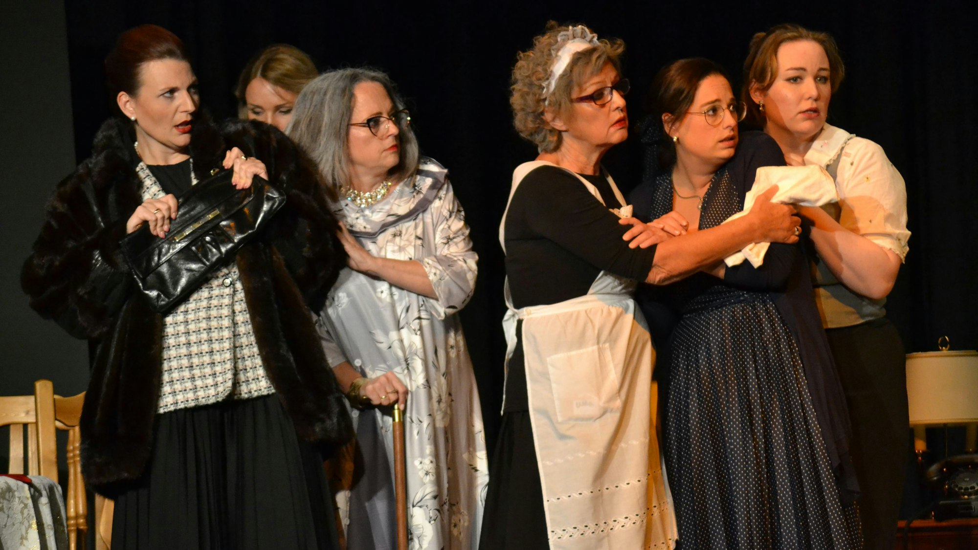 Dienstmädchen und vornehm gekleidete Frauen vor einem dunklen Bühnenhintergrund.