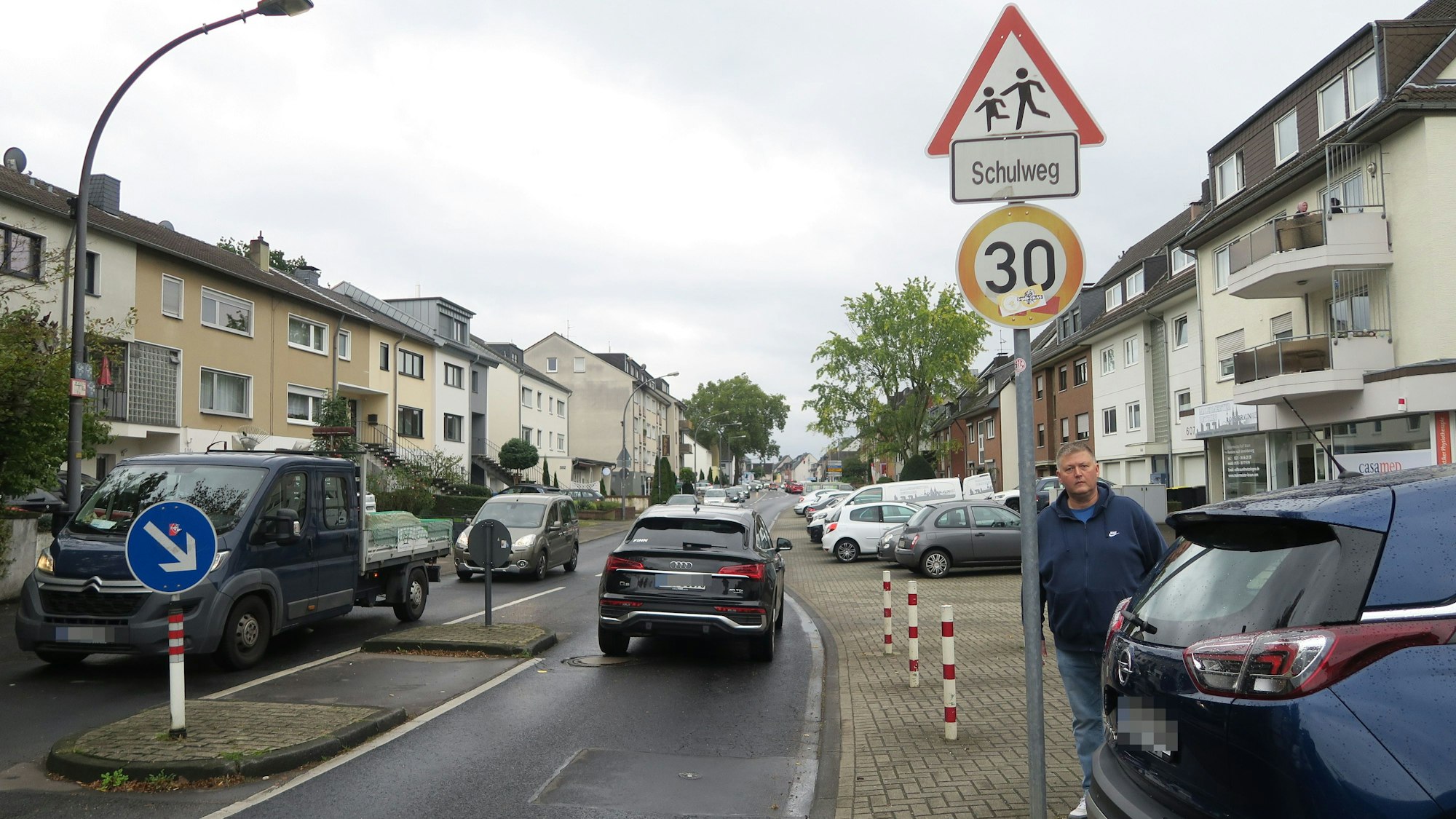 Ein Mann steht an einem Fußgängerüberweg. Autos fahren vorbei und parken am Straßenrand.