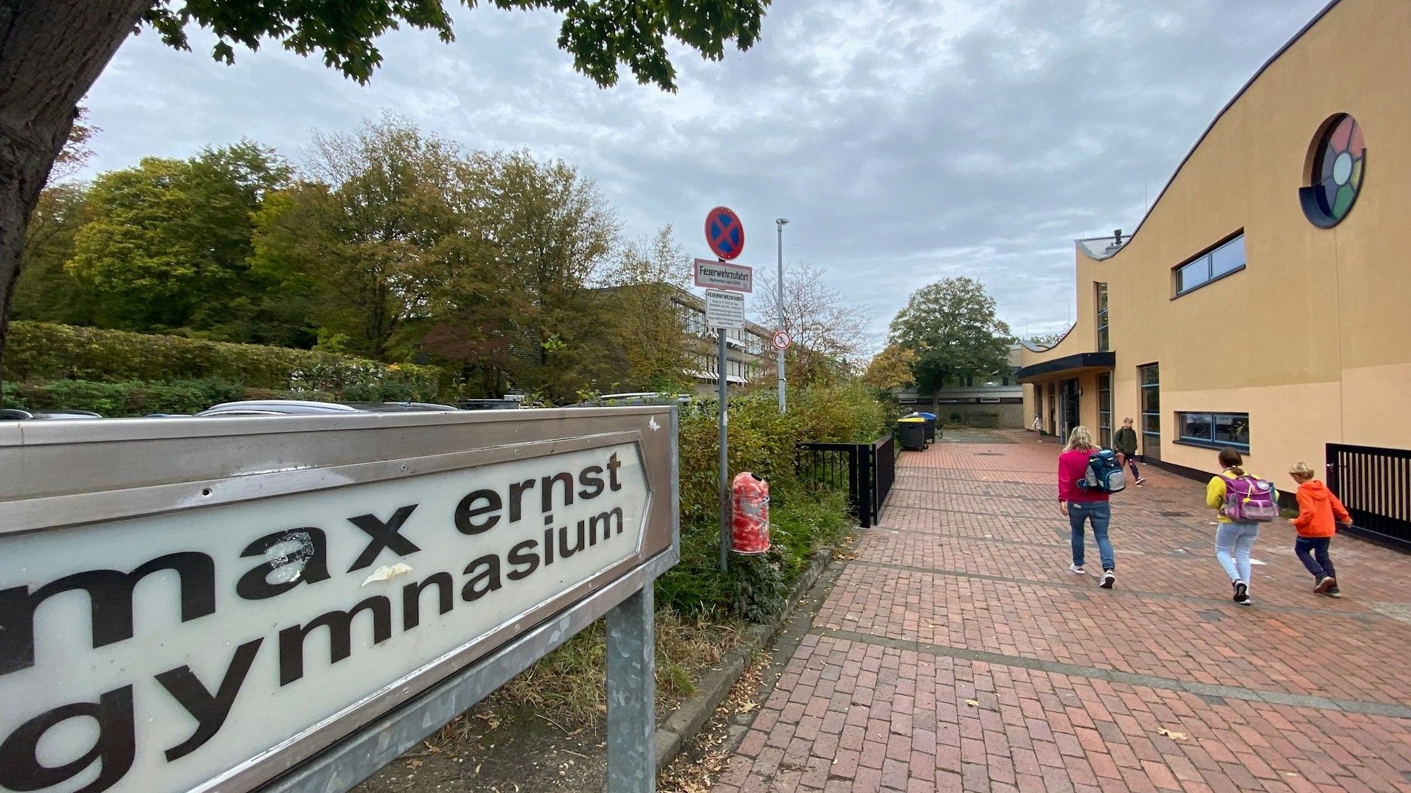 Zu sehen ist im Vordergrund ein Schild, das auf das Gymnasium im Hintergrund hinweist.