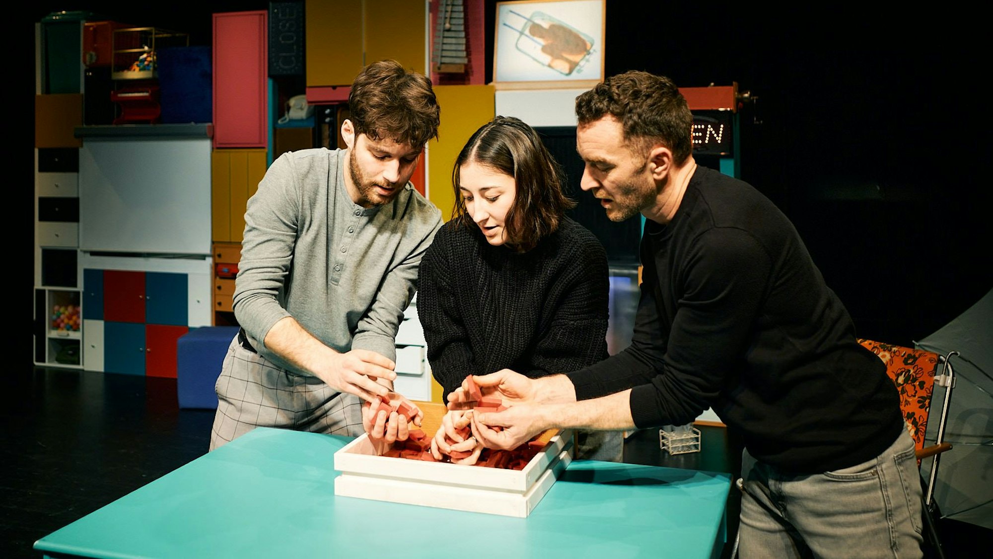 Drei Personen stehen an einem Tisch und greifen in eine Kiste