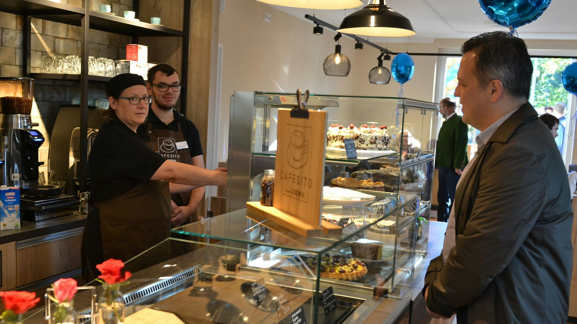 Euskirchens Bürgermeister Sacha Reichelt steht an einem Kuchentresen. Dahinter stehen Mitarbeiter des Cafésito.