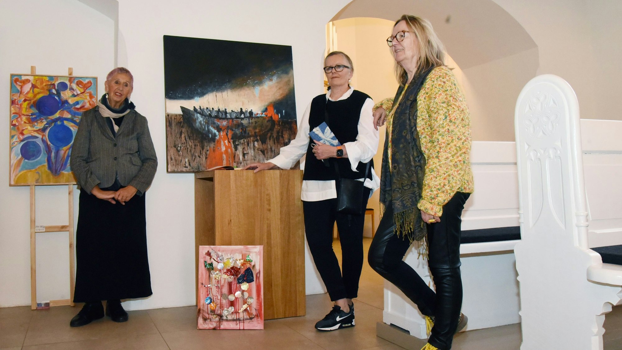 Drei Frauen stehen mit ihren Bildern zwischen Kirchenbänken.