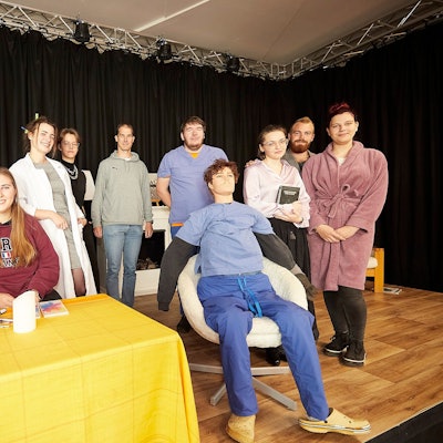 Eine Gruppe ehemaliger Schüler der Realschule Schleiden ist auf einer Bühne zu sehen. Dort proben sie für das Stück „Die Physikerinnen“.