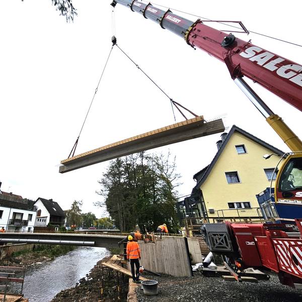 Ein Brückenteil hängt an zwei Seilen über der Urft in der Luft.