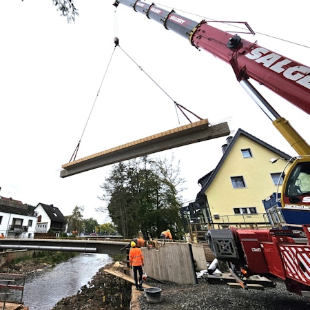 Ein Brückenteil hängt an zwei Seilen über der Urft in der Luft.