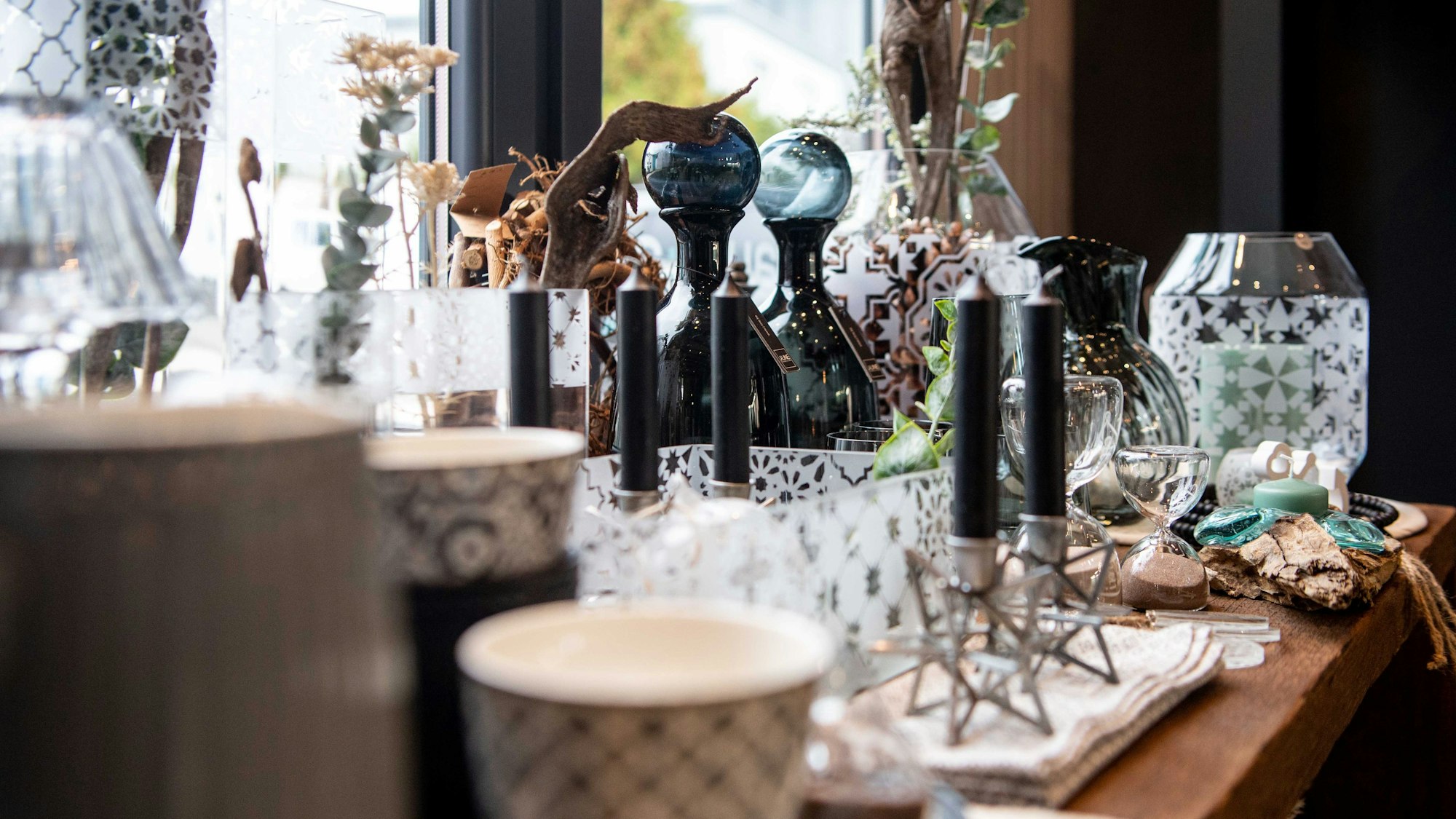 Kerzen, Gläser, Tassen, Trockenblumen und weitere Dekoartikel stehen auf einer Fensterbank.