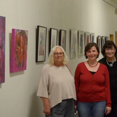 Die Künstlerinnen Donata Reinhard (v.l.), Petra Hansen und Beate Krupp stehen in einem der Flure des Euskirchener Rathauses, in denen sie ihre Werke ausstellen. Im Hintergrund hängen zahlreiche Bilder.