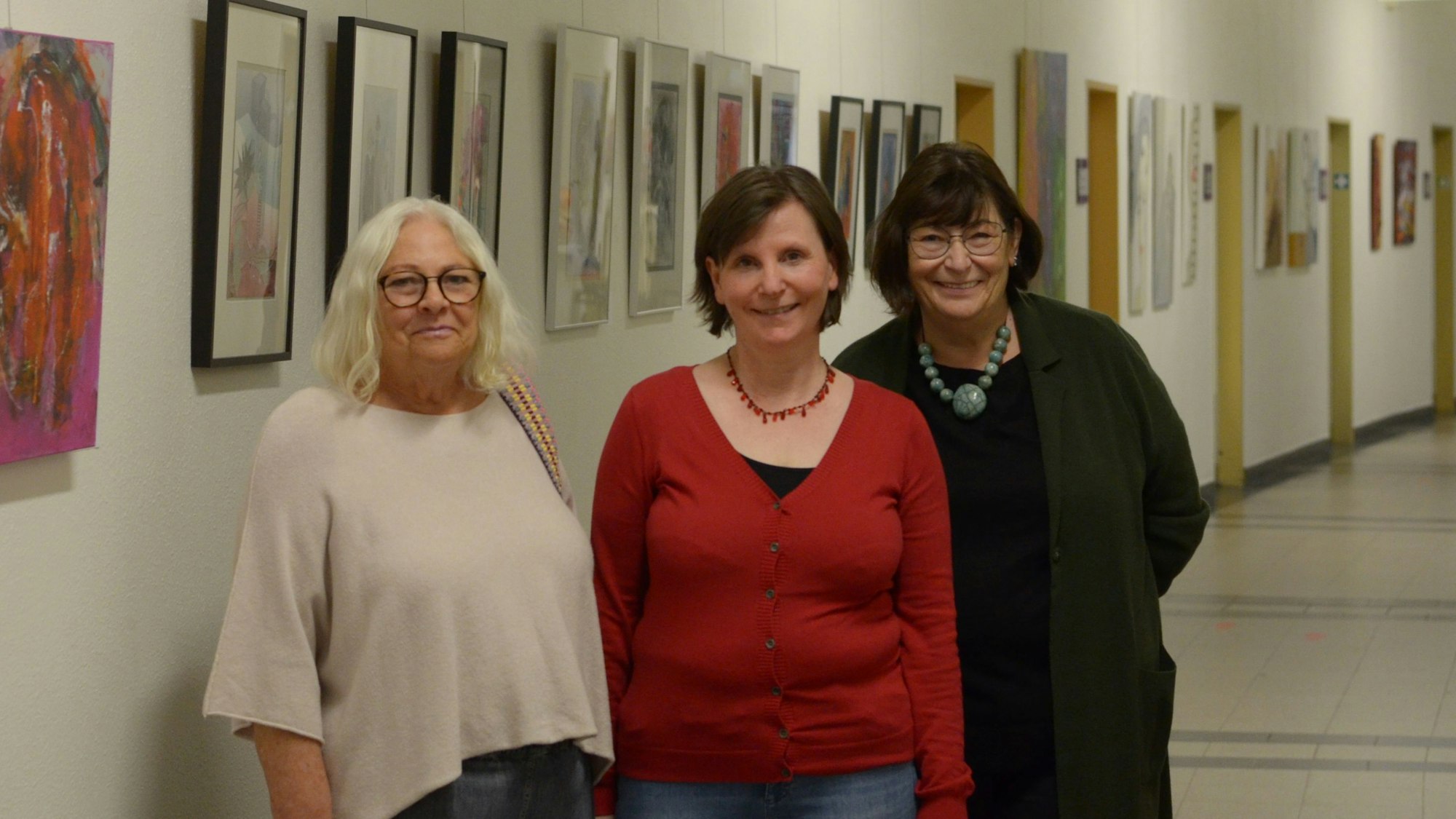 Die Künstlerinnen Donata Reinhard (v.l.), Petra Hansen und Beate Krupp stehen in einem der Flure des Euskirchener Rathauses, in denen sie ihre Werke ausstellen. Im Hintergrund hängen zahlreiche Bilder.