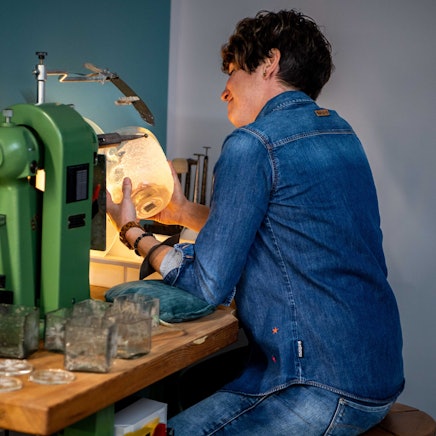 Kerstin Wexel nutzt eine Maschine, um Glas zu gestalten. Sie schaut dabei auf das Stück in Bearbeitung.