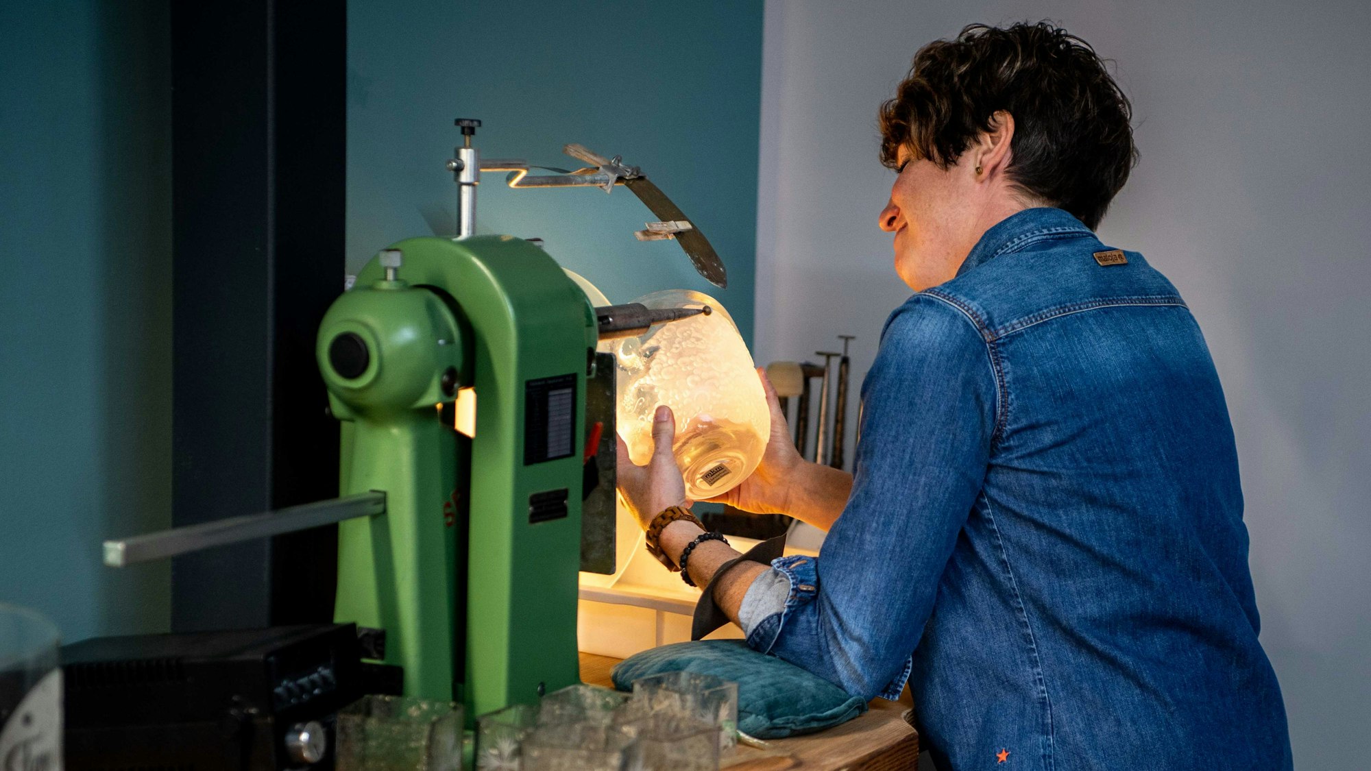 Kerstin Wexel nutzt eine Maschine, um Glas zu gestalten. Sie schaut dabei auf das Stück in Bearbeitung.