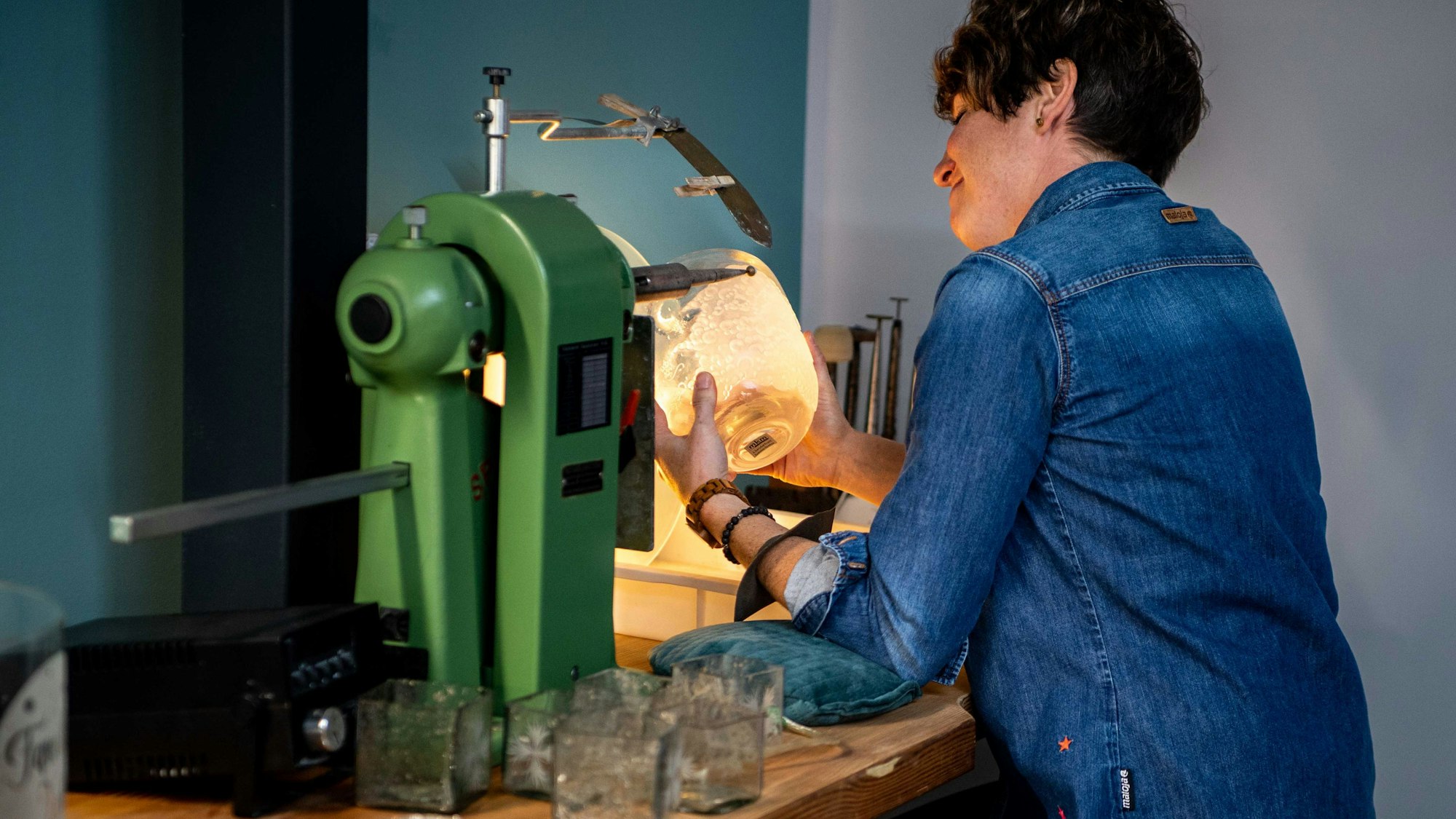 Die Glasveredlerin Kerstin Wexel sitzt an einem Spezialwerkzeug und graviert eine Glasvase.