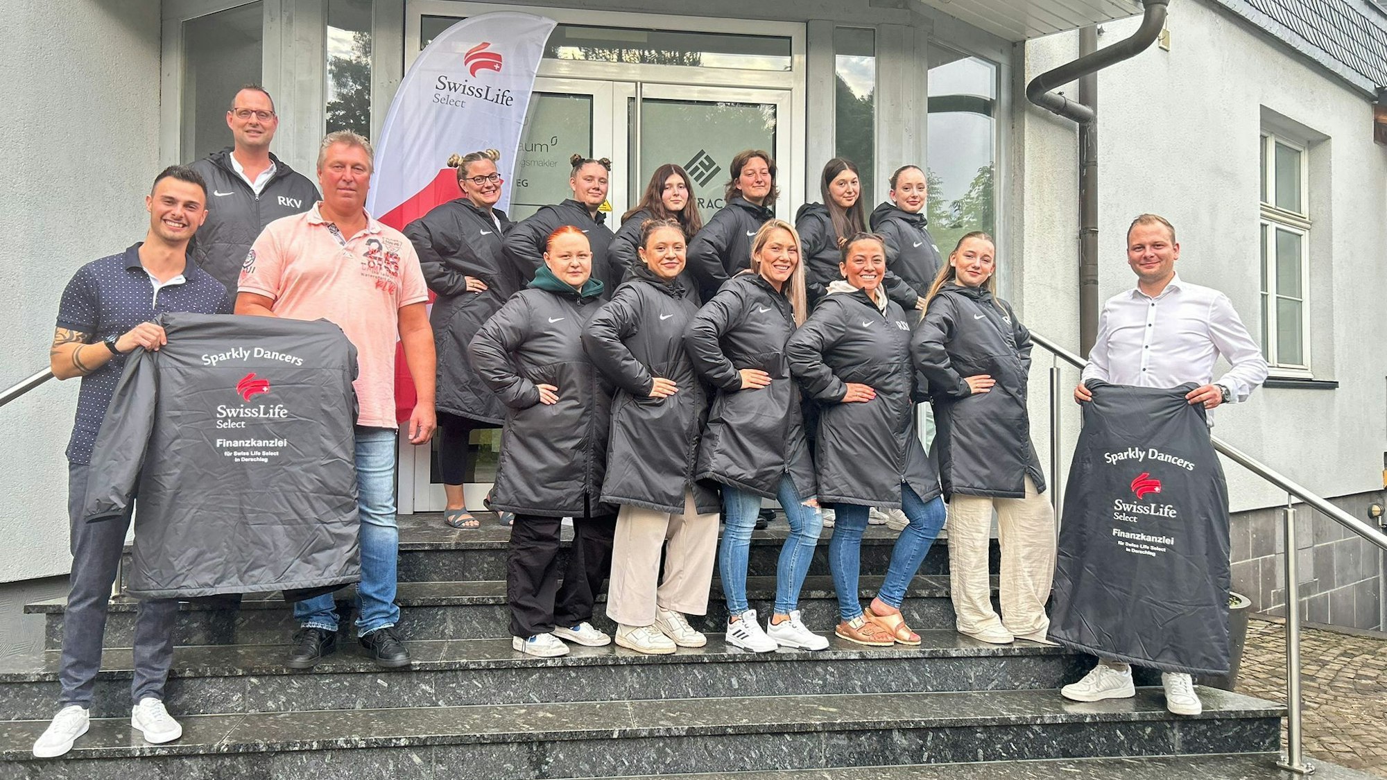 Eine Tanzgruppe steht für ein Gruppenbild gemeinsam auf Treppenstufen beisammen und präsentiert die neue gesponsorte Kleidung.